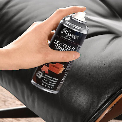 Hand spr&uuml;ht Pflegespray auf schwarzes Lederpolster, Dose &bdquo;Leather Spray&ldquo; von Hagerty.