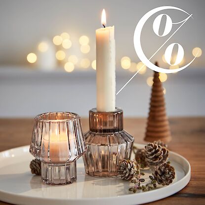 Teller mit zwei Windlichtern, brennender Kerze und Tannenzapfen, im Hintergrund warme Lichter und Prozentzeichen.