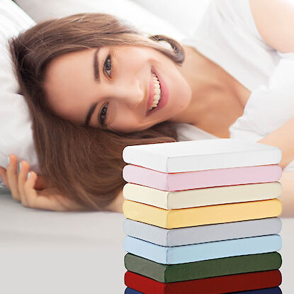 L&auml;chelnde Frau auf Bett mit Stapel bunter Spannbettlaken in verschiedenen Farben