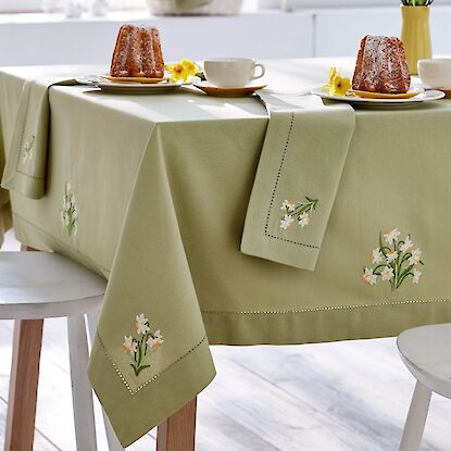 Gr&uuml;ne Tischdecke mit Blumenstickerei, gedeckter Tisch mit Kuchen, Tassen und passenden Servietten.
