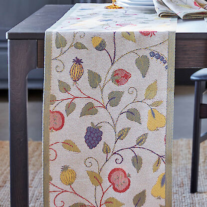 Tischl&auml;ufer mit farbigem Obst- und Blattmotiv auf gedecktem Tisch, dazu passende Servietten.