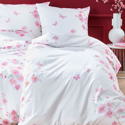 Wei&szlig;e Bettw&auml;sche mit rosa Bl&uuml;ten und Schmetterlingen, dekoriert vor roter Wand mit Vase und Zweigen.