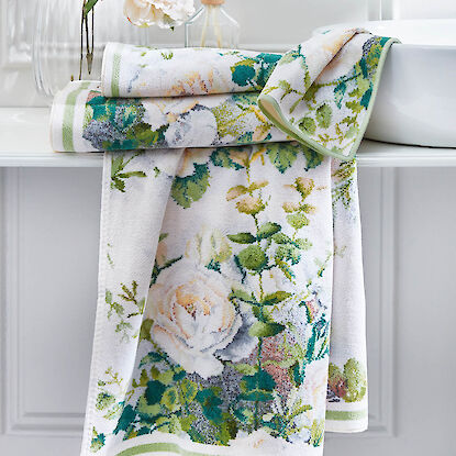 Wei&szlig;e Handt&uuml;cher mit floralem Muster in Gr&uuml;n- und Pastellt&ouml;nen, dekorativ im Bad arrangiert.