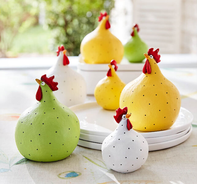 Dekorative H&uuml;hnerfiguren in Gelb, Gr&uuml;n und Wei&szlig; mit Punkten, arrangiert auf Tisch und Tellern
