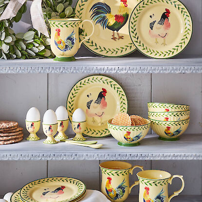 Gelbes Geschirr mit Hahnen- und Hennenmotiven im Regal arrangiert, inklusive Tassen, Tellern und Eierbechern.