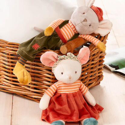 Zwei Pl&uuml;schm&auml;use in bunter Kleidung sitzen an einem Flechtkorb und liegen auf dem Holzboden.