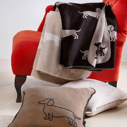Decken und Kissen mit Dackelmotiven auf rotem Sessel und Boden arrangiert.
