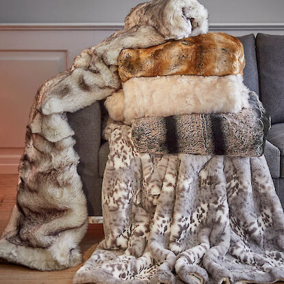 Weiche Kunstfelldecken in verschiedenen Naturt&ouml;nen, &uuml;bereinander auf dem Sofa drapiert.