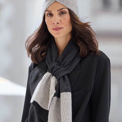 Frau tr&auml;gt graues Stirnband und zweifarbig gestrickten Schal &uuml;ber schwarzem Mantel im Winterlook.