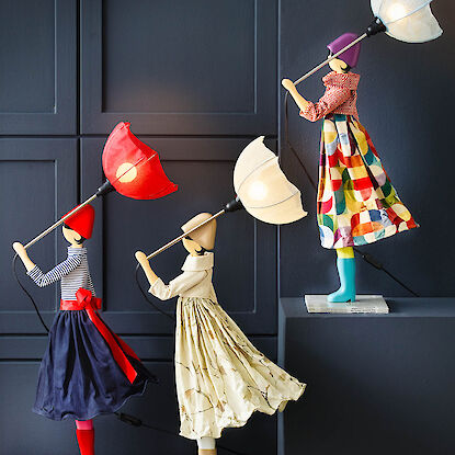 Drei Lampenfiguren als Frauen mit Schirmen, deren leuchtende Schirme als Lampen dienen.