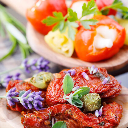 Tomates s&eacute;ch&eacute;es avec herbes, c&acirc;pres et fleurs de lavande sur cuill&egrave;re en bois, derri&egrave;re poivrons farcis avec persil.