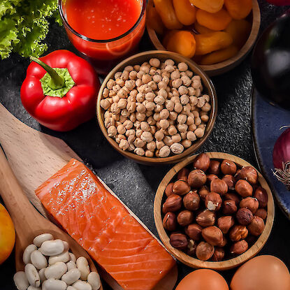 S&eacute;lection d&rsquo;ingr&eacute;dients frais : saumon, pois chiches, noix, haricots, poivron, salade, abricots, &oelig;ufs et jus de tomate sur fond sombre.