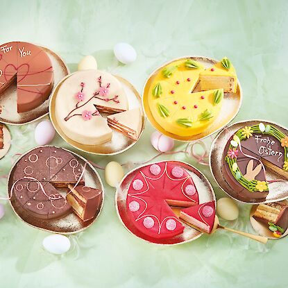 Assortiment de g&acirc;teaux de P&acirc;ques color&eacute;s sur assiettes dor&eacute;es, d&eacute;cor&eacute;s de massepain et chocolat, chacun avec une part.