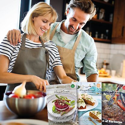 Couple cuisinant ensemble en d&eacute;coupant des l&eacute;gumes, avec quatre couvertures de livrets de recettes Hagen Grote affich&eacute;es.