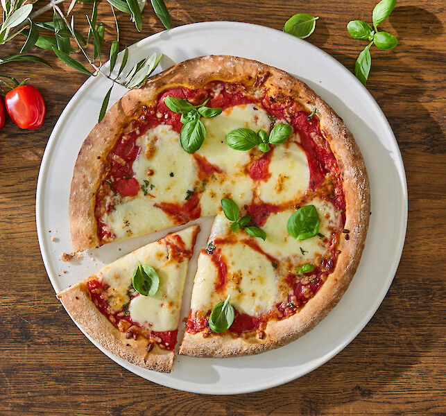 Pizza Margherita sur assiette, mozzarella fondue et feuilles de basilic, une part d&eacute;coup&eacute;e.