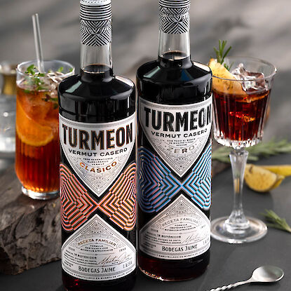 Deux bouteilles de vermouth Turmeon devant des cocktails avec glace, agrumes et herbes sur fond sombre.