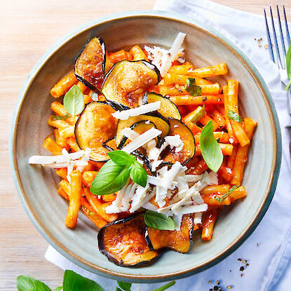 P&acirc;tes &agrave; la sauce tomate avec aubergines grill&eacute;es et fromage r&acirc;p&eacute;, garnies de basilic dans un bol.