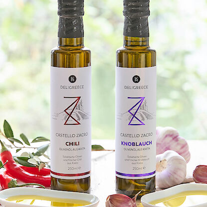 Deux bouteilles d&rsquo;huile d&rsquo;olive chili et ail de Deligreece, entour&eacute;es de piments frais, d&rsquo;ail et de coupelles d&rsquo;huile.