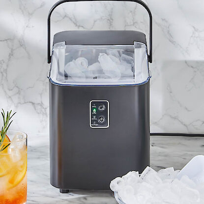 Machine &agrave; gla&ccedil;ons compacte sur marbre, remplie de glace, avec bol de gla&ccedil;ons et verre de boisson aux agrumes.