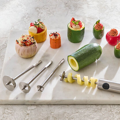 Coupe-l&eacute;gumes avec embouts, courgettes, carottes et oignons &eacute;vid&eacute;s et farcis, dispos&eacute;s sur une plaque en marbre.