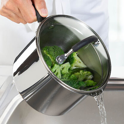 Personne &eacute;gouttant l&rsquo;eau chaude d&rsquo;une casserole avec brocoli, couvercle entrouvert, au-dessus de l&rsquo;&eacute;vier.