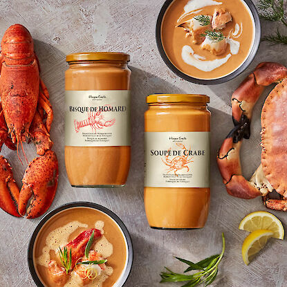 Deux bocaux de soupe de homard et de crabe, servis en bols garnis, entour&eacute;s de homard, crabe, citron et herbes fra&icirc;ches.