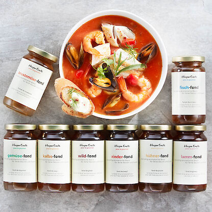 Divers fonds Hagen Grote devant un bol de soupe aux fruits de mer, avec pain et herbes sur surface pierre claire.