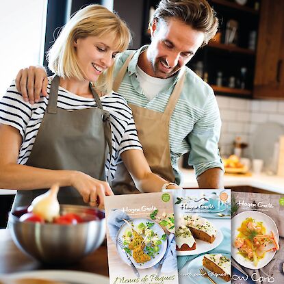 Couple cuisinant ensemble en d&eacute;coupant des l&eacute;gumes, avec quatre couvertures de livrets de recettes Hagen Grote affich&eacute;es.