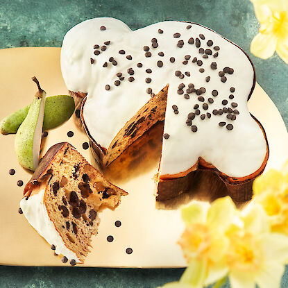 Osterkuchen in Kleeblattform mit wei&szlig;er Glasur und Schokotropfen, angeschnitten, mit Birnen dekoriert serviert.