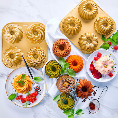 Goldfarbene Backformen mit verschiedenen Gugelhupf-Motiven, daneben gebackene Mini-Gugelhupfe und Desserts dekorativ arrangiert.