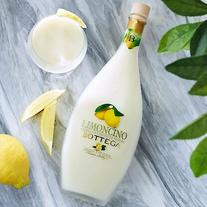 Cremiger Limoncello aus Sizilien in eleganter Flasche, mit Zitronenscheiben und eingeschenktem Lik&ouml;r auf Marmorfl&auml;che.