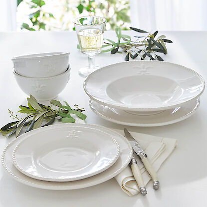 Elegantes wei&szlig;es Tafelservice mit Tellern und Schalen, dekoriert mit Olivenzweigen, Besteck und Glas auf hellem Tisch.