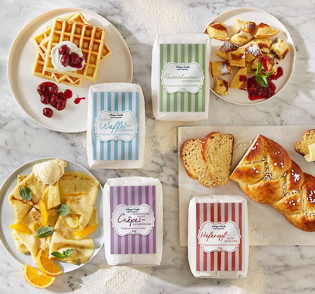 Backmischungen f&uuml;r Waffeln, Kaiserschmarrn, Cr&ecirc;pes und Hefezopf, arrangiert mit frisch gebackenem Geb&auml;ck auf Marmorfl&auml;che.