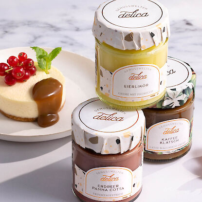 Dessertaufstriche im Glas: Eierlik&ouml;rcreme, Erdbeer-Panna-Cotta und Kaffeecreme, arrangiert neben kleinem Kuchen auf hellem Tisch.