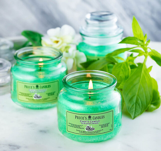 Gr&uuml;ne Duftkerzen im Glas mit brennender Flamme, dekoriert mit Basilikumbl&auml;ttern und wei&szlig;en Bl&uuml;ten auf hellem Untergrund.