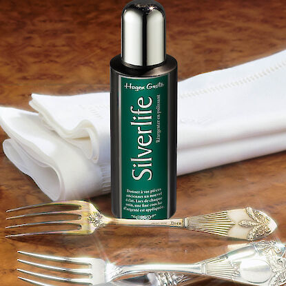 Flasche Hagen Grote Silverlife Silberpflege steht auf Holztisch neben poliertem Besteck und wei&szlig;em Tuch.