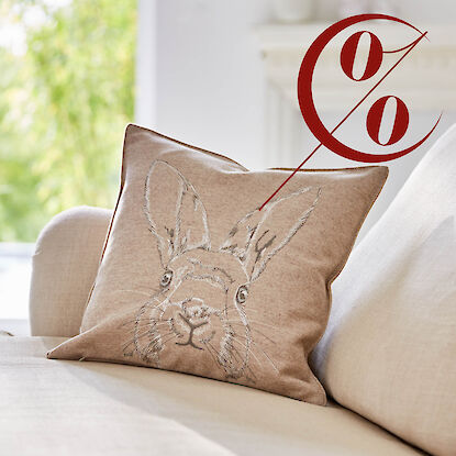 Beiges Dekokissen mit einer Illustration eines Hasenkopfs mit braunen und wei&szlig;en Linien im Stil einer Skizze in einer Sofaecke mit hellem Bezug