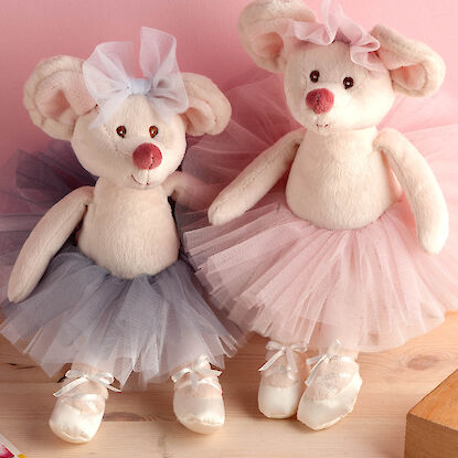 Zwei Pl&uuml;schm&auml;use in bunter Kleidung sitzen an einem Flechtkorb und liegen auf dem Holzboden.