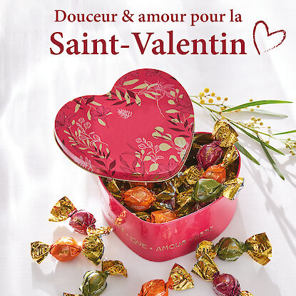 Bo&icirc;te cadeau en forme de c&oelig;ur remplie de chocolats emball&eacute;s or, ouverte sur fond clair, pour la Saint-Valentin.