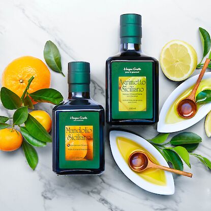 Deux bouteilles d&rsquo;huile d&rsquo;olive aromatis&eacute;e de Sicile aux agrumes, entour&eacute;es d&rsquo;oranges, citrons et feuilles fra&icirc;ches