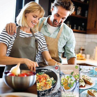 Paar kocht gemeinsam in der K&uuml;che, schneidet Gem&uuml;se, daneben Hagen-Grote-Rezepthefte mit saisonalen Gerichten