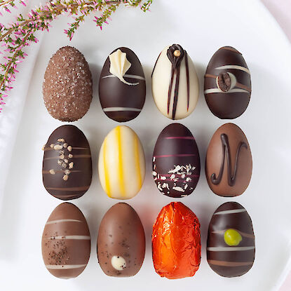 Auswahl handgefertigter Schokoladen-Ostereier mit unterschiedlichen Glasuren und Dekoren, auf wei&szlig;em Teller arrangiert