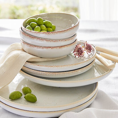 Vaisselle en c&eacute;ramique empil&eacute;e aux tons naturels, bols et assiettes d&eacute;cor&eacute;s d&rsquo;olives vertes et d&rsquo;une serviette en tissu