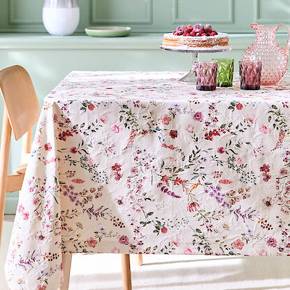 Table dress&eacute;e avec nappe &agrave; motifs floraux, g&acirc;teau sur pr&eacute;sentoir et verres color&eacute;s, ambiance printani&egrave;re lumineuse
