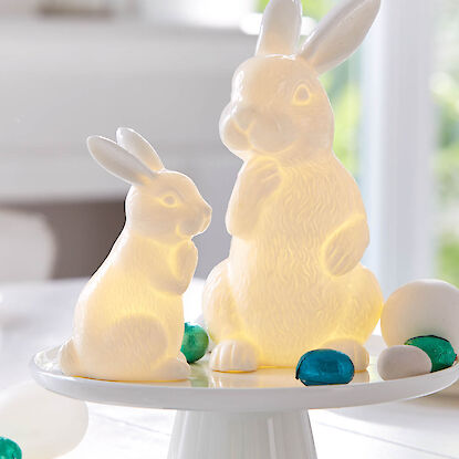 Lapins de P&acirc;ques lumineux en verre sur pr&eacute;sentoir, d&eacute;cor&eacute;s d&rsquo;&oelig;ufs, d&eacute;coration pascale chaleureuse