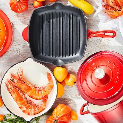 Batterie de cuisine en fonte color&eacute;e avec cocotte, po&ecirc;le grill et faitout, dispos&eacute;e avec crevettes et l&eacute;gumes, vue de dessus