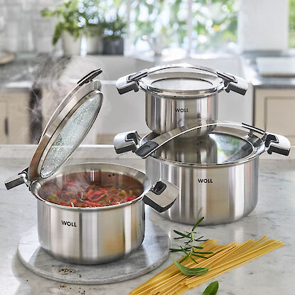 Casseroles en acier inoxydable avec couvercles en verre sur plan de travail, une marmite ouverte avec plat fumant