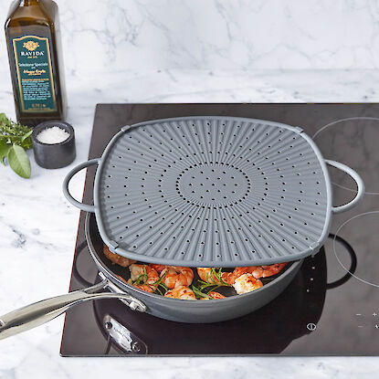 Po&ecirc;le sur plaque &agrave; induction avec crevettes et herbes, couverte d&rsquo;un pare-&eacute;claboussures perfor&eacute;