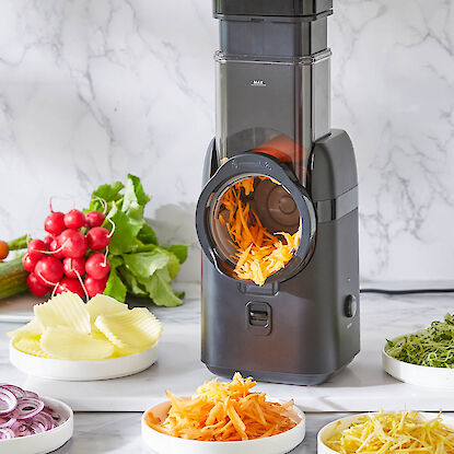 R&acirc;pe &eacute;lectrique avec tambour rotatif, r&acirc;pant des carottes, entour&eacute;e de l&eacute;gumes fra&icirc;chement d&eacute;coup&eacute;s