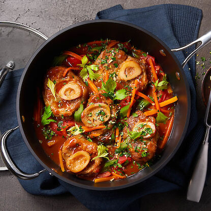 Jarrets brais&eacute;s en sauce cors&eacute;e avec l&eacute;gumes et herbes, servis dans une cocotte noire, vue de dessus